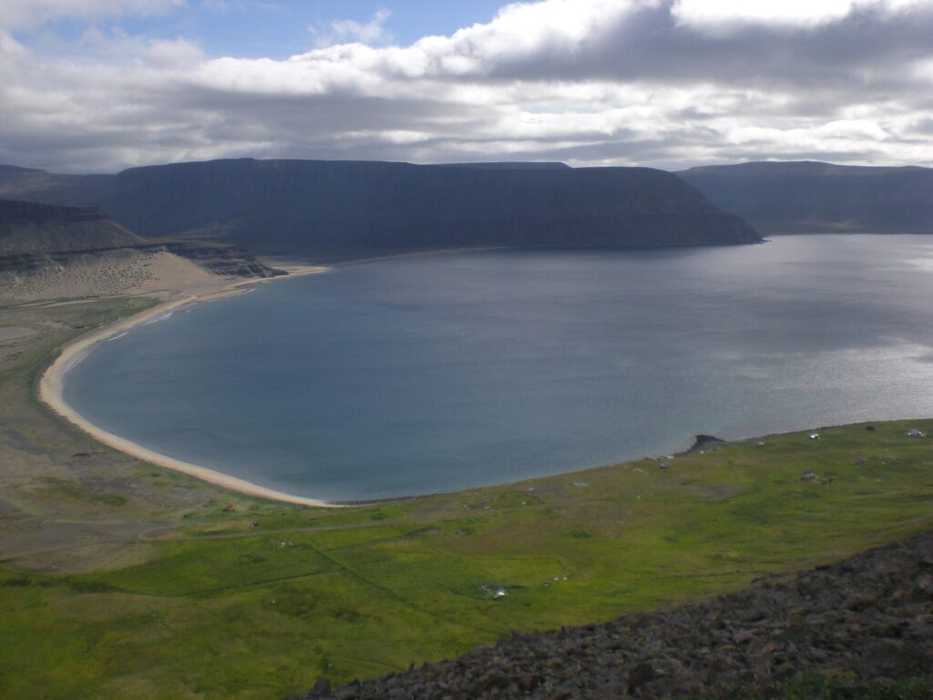 The broad bay of Aðalvík in Hornstrandir, Iceland, with grassy shoreline and mountains behind.