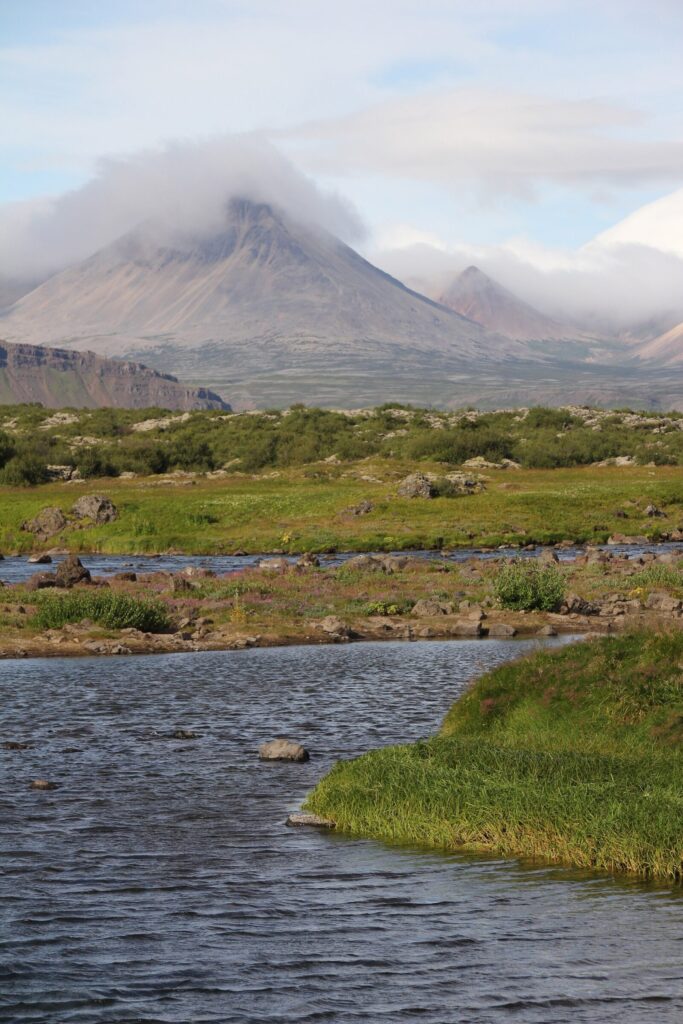 The pale orange rhyolite cone of Baula mountain rising above the Norðurá river valley in West Iceland under a partly cloudy sky.