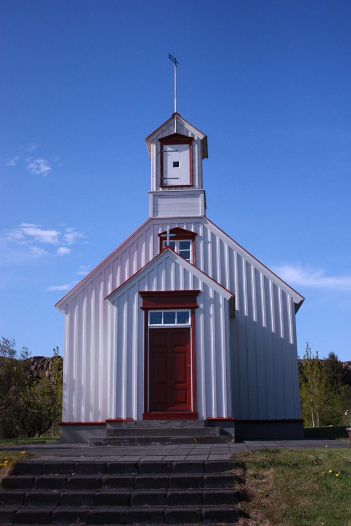 The small white church with a dark roof at Borg á Mýrum near Borgarnes, West Iceland, standing on open ground under a cloudy sky.