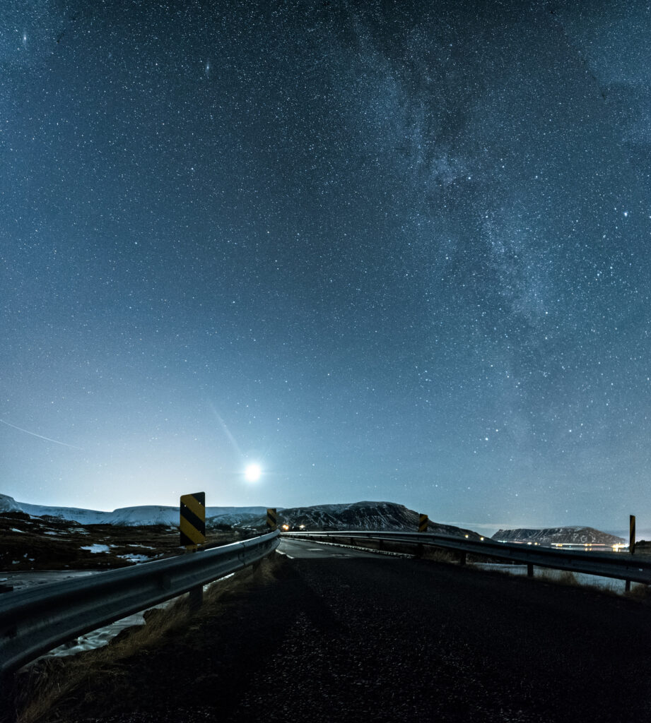 The Milky Way arching across a dark winter night sky over an Icelandic bridge, with the moon low on the horizon.