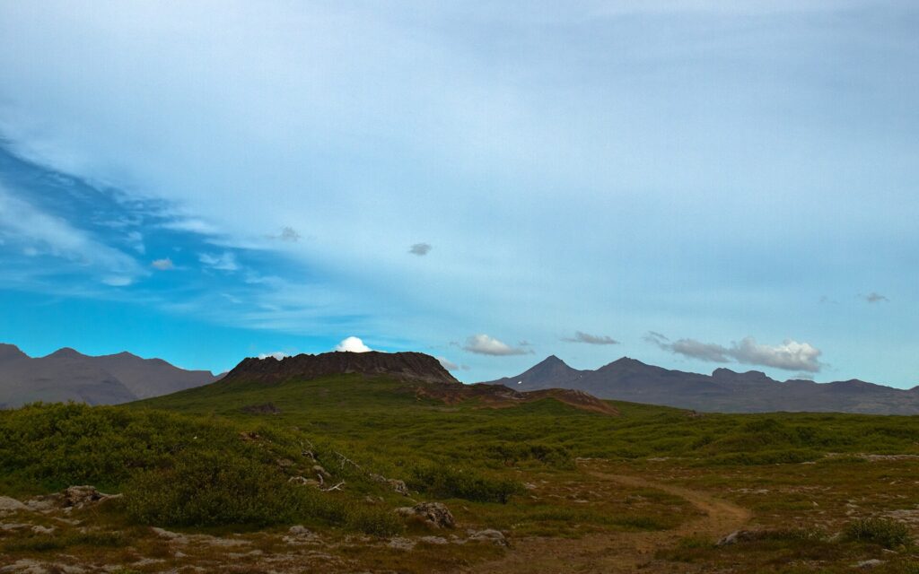 The oval Eldborg spatter cone rising low above the flat lava fields of Mýrar in West Iceland, with mountains in the distance.