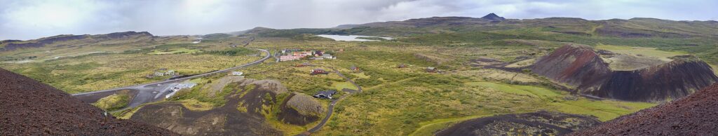 Panoramic view of the Litli Grábrók crater in Vesturland, West Iceland, its reddish volcanic bowl set in a green lava field under a bright sky.