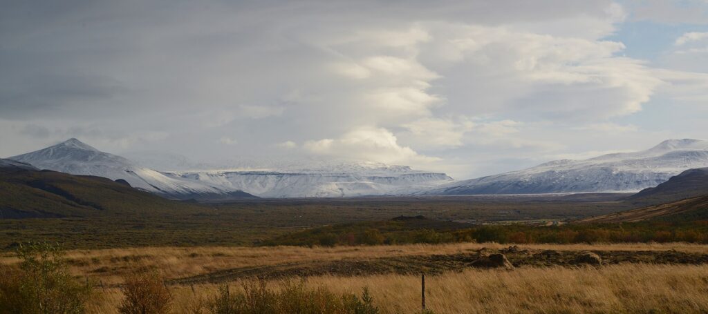 Panoramic view of the highland terrain above Húsafell, West Iceland, with volcanic slopes and the glacier Eiríksjökull under a cloudy sky.