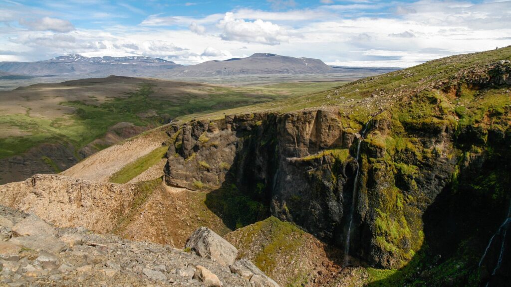 Wooded river valley near Húsafell in West Iceland, with birch scrub, grassy slopes and a glacial river running through the landscape.