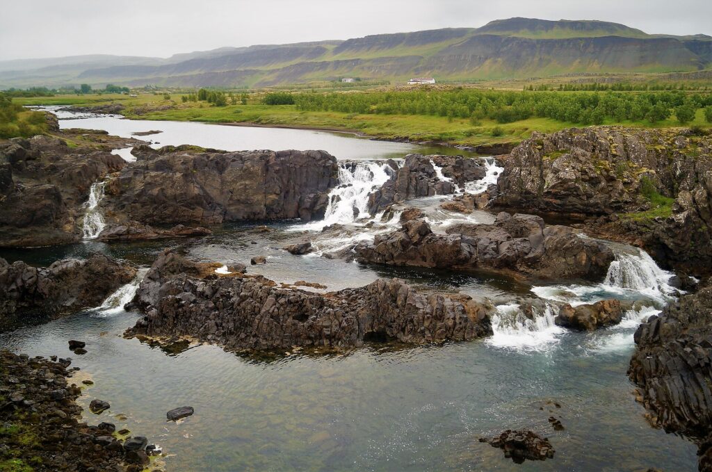 Glanni waterfall cascading over dark rock ledges on the Norðurá river amid green lava-field vegetation in Borgarfjörður, West Iceland.