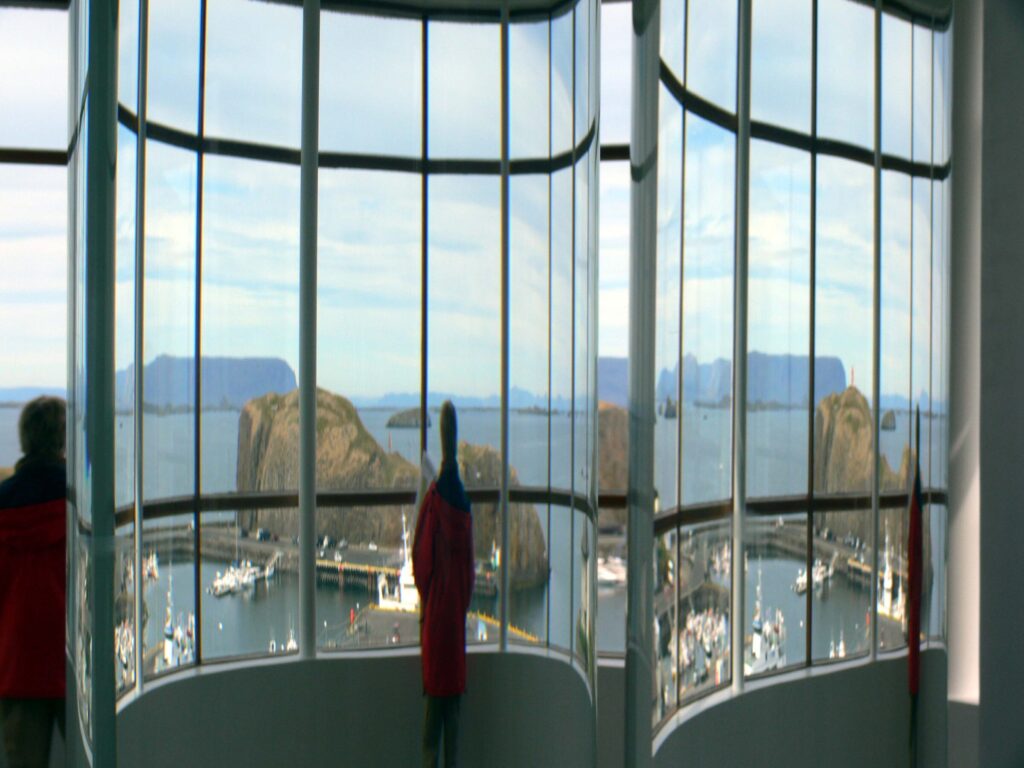 Interior of the Library of Water in Stykkishólmur showing floor-to-ceiling glass columns filled with glacial water, with harbour views through the windows behind