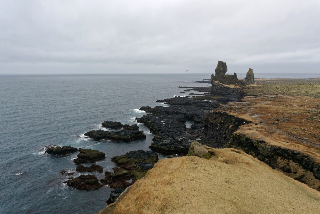 Two tall basalt sea stacks of Lóndrangar rising from a grassy coastal field on the Snæfellsnes Peninsula in Iceland