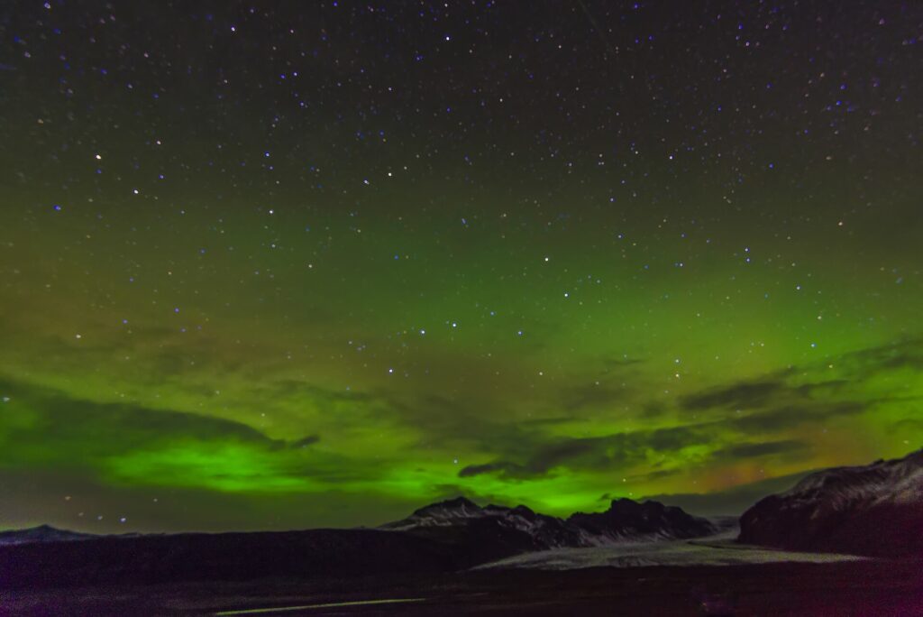 Green aurora borealis swirling across a dark night sky over the Icelandic countryside.