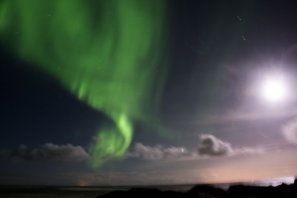 Green aurora borealis glowing over the harbour and hillside at Stykkishólmur, Iceland, at night