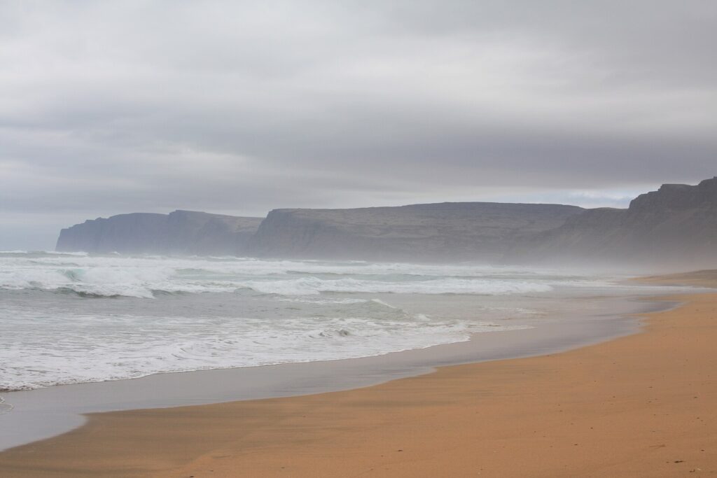 Wide view of Rauðasandur beach in the Westfjords, showing the long red-gold sand flats and green farmland behind