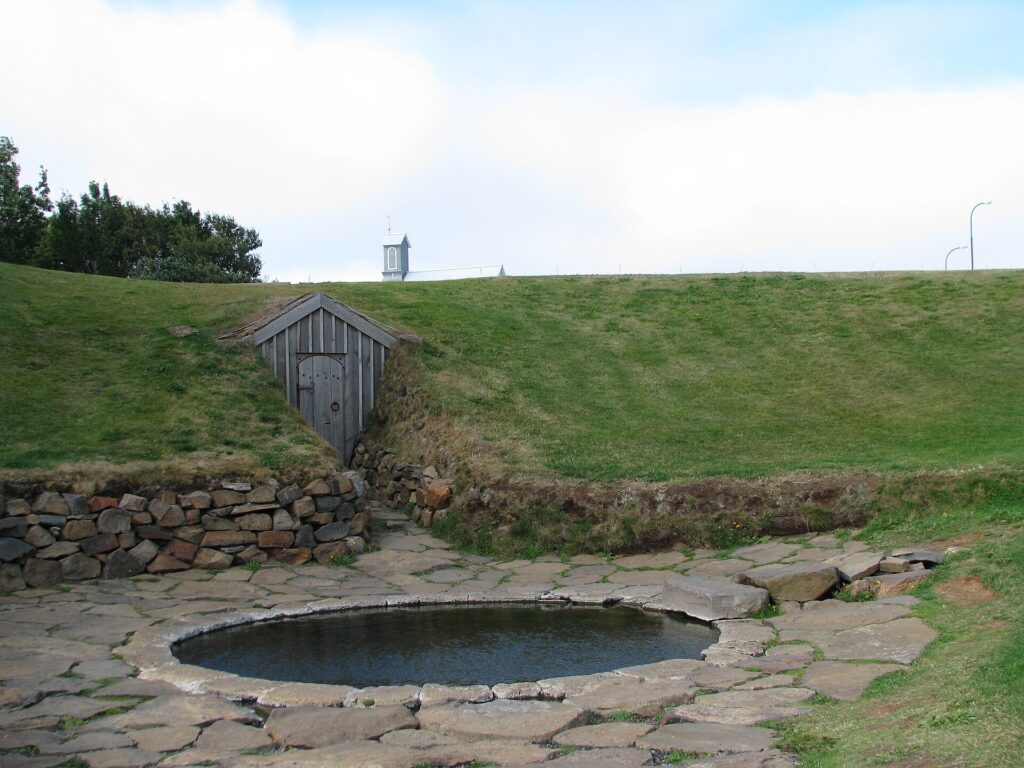 The circular stone-lined Snorralaug geothermal pool at Reykholt, West Iceland, with grass and a low turf slope behind it.