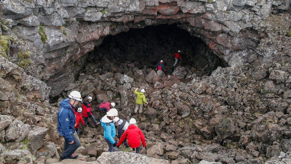 The rocky, undeveloped interior of Surtshellir lava cave in Iceland, with jumbled lava-block walls and floor lit from the entrance opening.