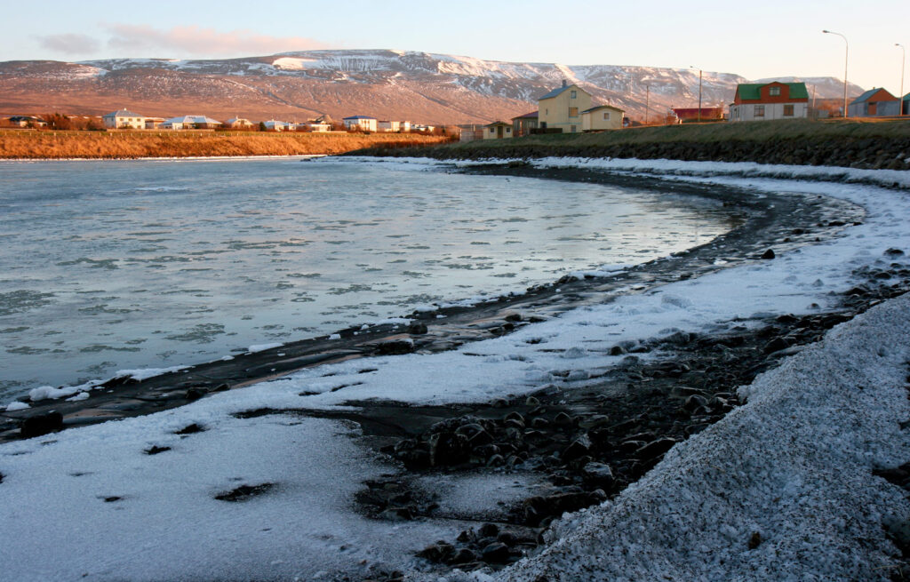 An Icelandic river flowing through a snow-dusted winter landscape under an overcast November sky at Blönduós, Iceland.